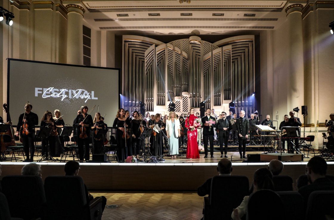 Zespół artystów, solistów i muzyków orkiestry Filharmonii Krakowskiej stoi na scenie podczas finału koncertu „Siła słowa” w ramach Festiwalu „Cały Twój”. W tle monumentalne organy oraz ekran z logo festiwalu. Publiczność widoczna na pierwszym planie bije