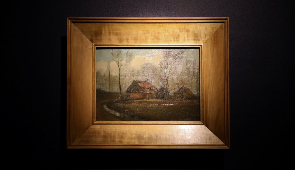 "Obraz Vincenta van Gogha przedstawiający wiejskie chaty pośród drzew, utrzymany w ciemnej, stonowanej kolorystyce. Na pierwszym planie widoczna jest kręta ścieżka prowadząca do dwóch domów z czerwonymi dachami. W tle wznoszą się bezlistne drzewa na tle zachmurzonego nieba. Obraz znajduje się w prostokątnej, drewnianej ramie i jest wyeksponowany na ciemnej ścianie galerii."