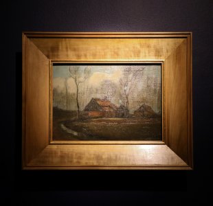 "Obraz Vincenta van Gogha przedstawiający wiejskie chaty pośród drzew, utrzymany w ciemnej, stonowanej kolorystyce. Na pierwszym planie widoczna jest kręta ścieżka prowadząca do dwóch domów z czerwonymi dachami. W tle wznoszą się bezlistne drzewa na tle zachmurzonego nieba. Obraz znajduje się w prostokątnej, drewnianej ramie i jest wyeksponowany na ciemnej ścianie galerii."