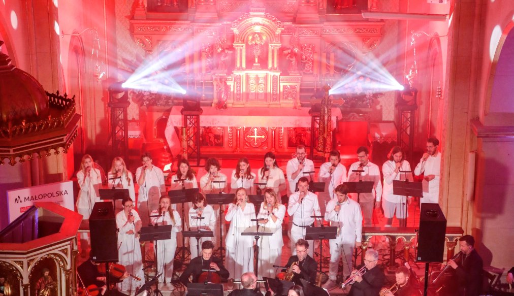 Solistka Izabela Szafrańska w czasie śpiewu, za nią muzycy, na dalszym planie chór.